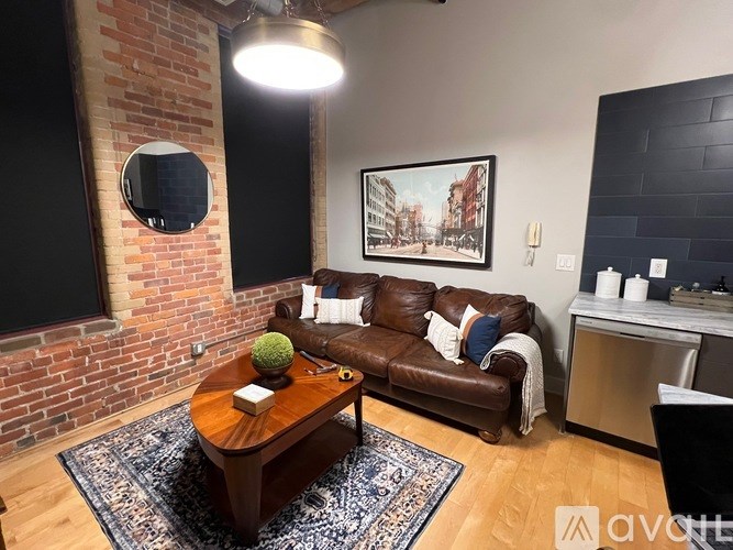 A living room with a brown leather couch and a coffee table in front of a brick wall.