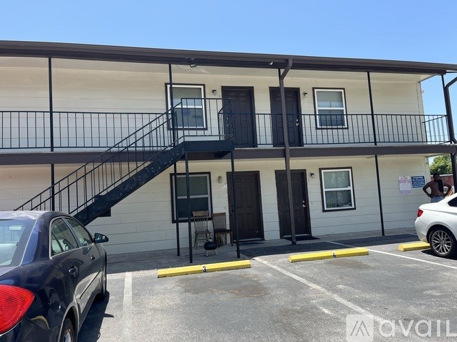 A black car is parked in a parking lot in front of a two-story building.