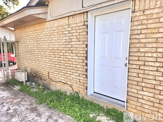 A white door is on a brick wall with a small garden in front.
