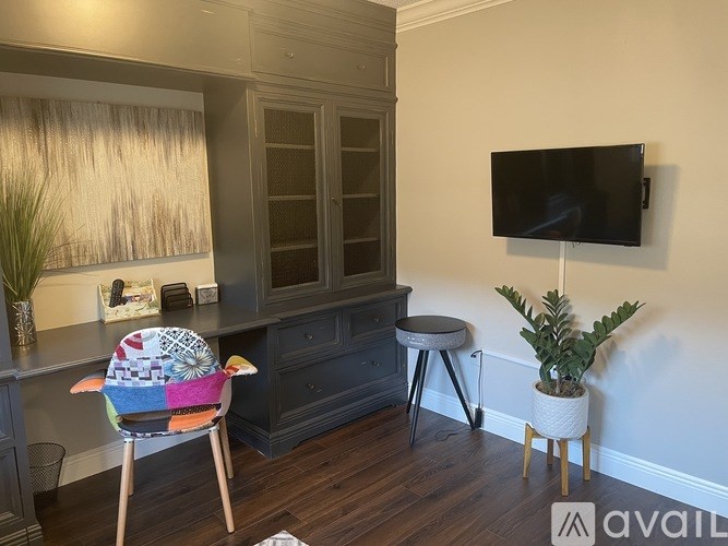 A room with a chair, a table, a plant and a television.