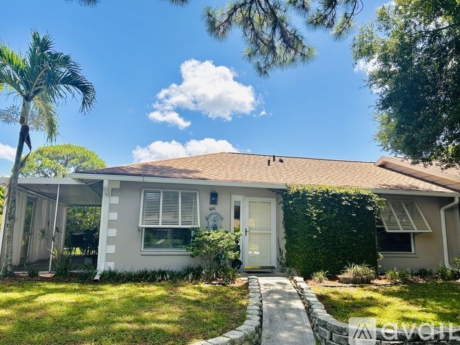 A house with a white exterior and a brown roof is surrounded by greenery.