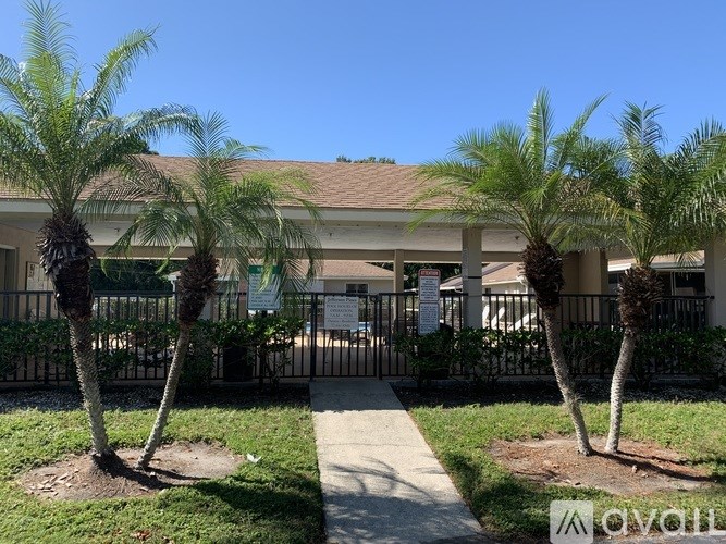 A building with a fence and three palm trees in front.