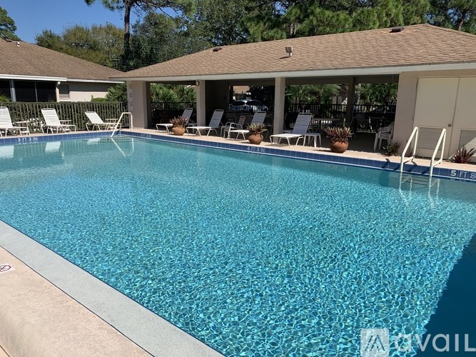 A pool with a white chair and a brown roofed building in the background.