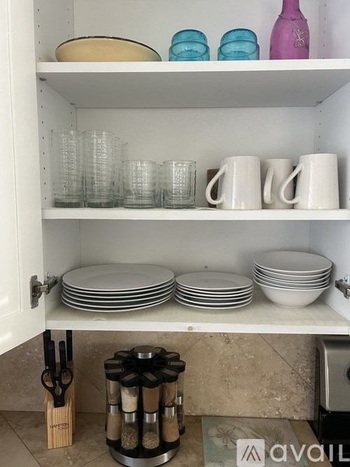 A kitchen cabinet with plates, cups, and a pepper grinder.