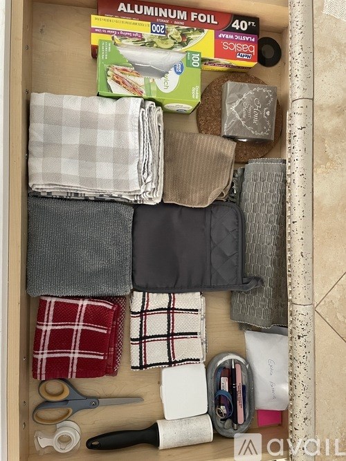 A drawer full of various items including a pair of scissors, a roll of tape, and a box of aluminum foil.