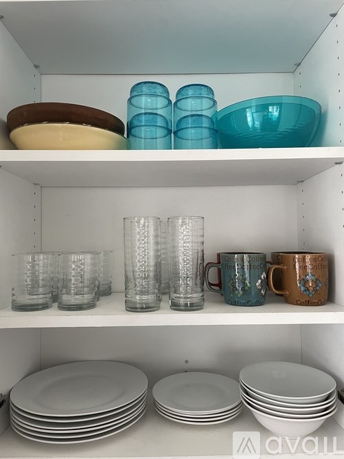 A white shelf with plates and glasses on it.