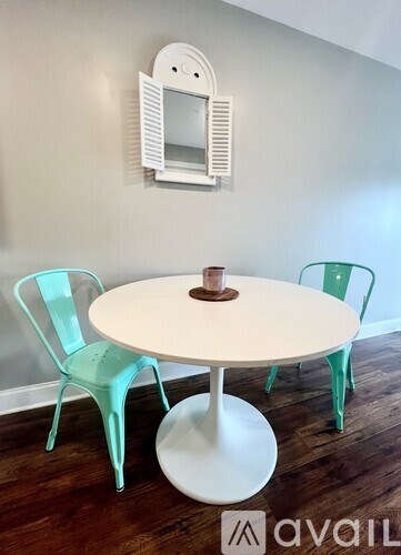A white table with a round base and a white chair with a green chair and a white wall with a mirror.