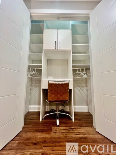A small white closet with a desk and chair in the middle.