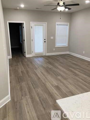 A room with a ceiling fan and light, wooden flooring, and two doors.