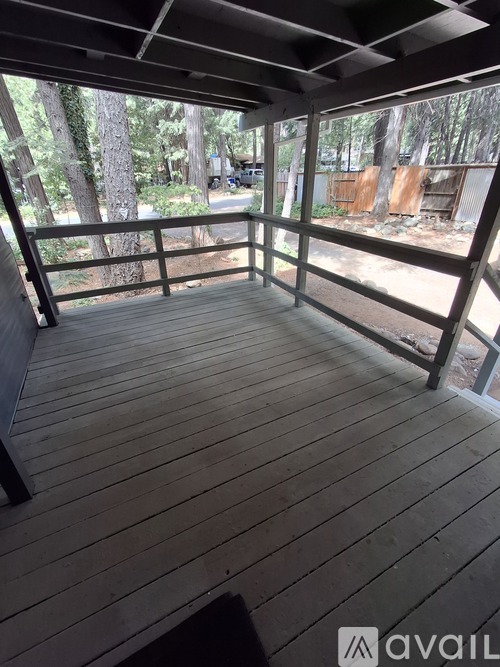 A wooden deck with a railing and a view of trees and a fence.