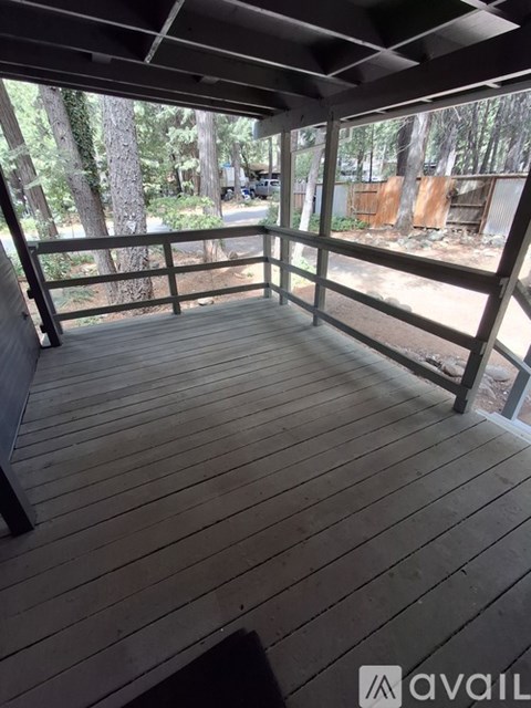 A wooden deck with a railing and a view of trees and a fence.