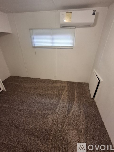 A carpeted room with a window and an air conditioner.