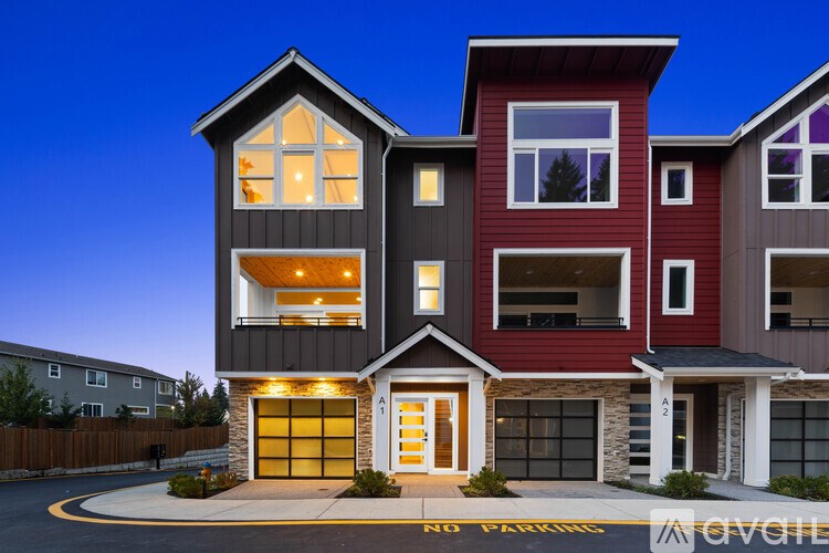 A modern two-story house with a red and grey exterior is shown at dusk.
