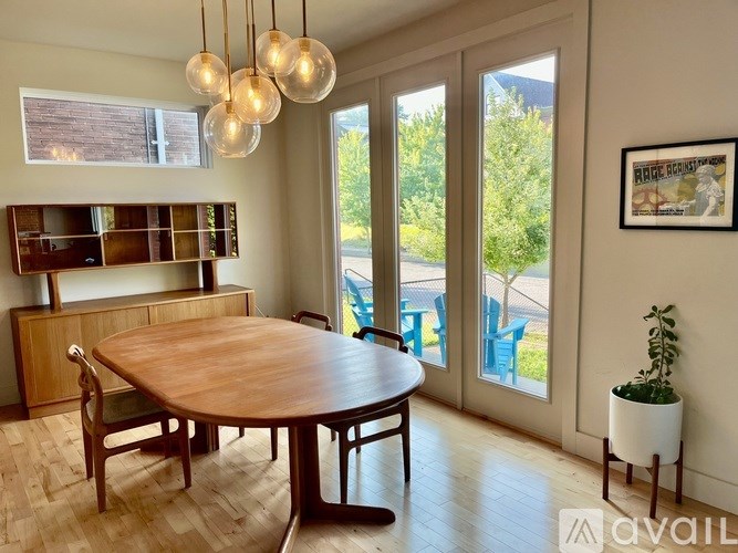 A dining room with a wooden table and chairs, a plant, and a framed picture on the wall.