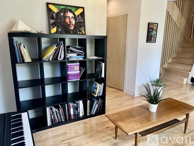 A room with a piano, a bookshelf, a coffee table and a staircase.