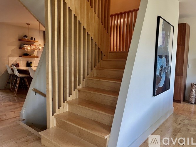 A wooden staircase with a white wall on one side and a painting hanging on the wall.