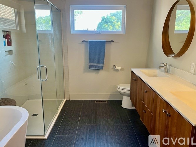 A bathroom with a glass shower stall, a toilet, a sink, and a window.
