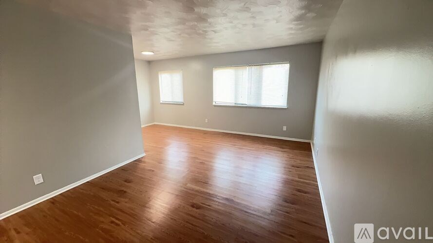A room with wooden flooring and two windows.