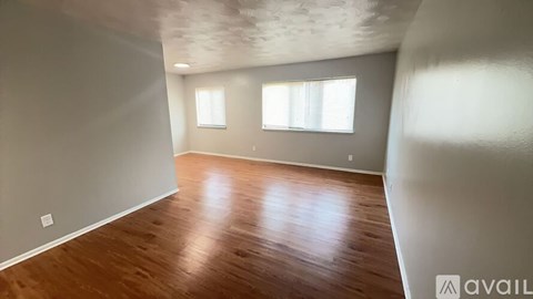 A room with wooden flooring and two windows.