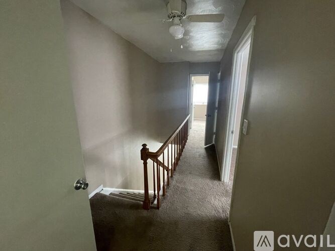 A hallway with a carpeted floor and a wooden staircase.