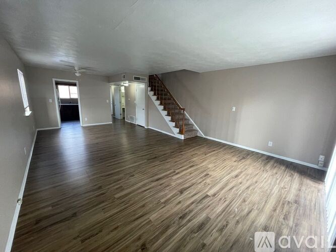A spacious room with wooden flooring and a staircase.