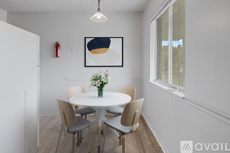 A dining room with a white table and chairs, a framed picture on the wall, and a vase of flowers on the table.