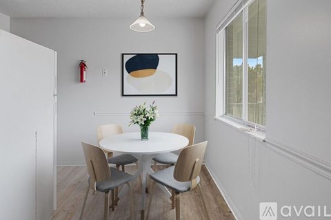 A dining room with a white table and chairs, a framed picture on the wall, and a vase of flowers on the table.