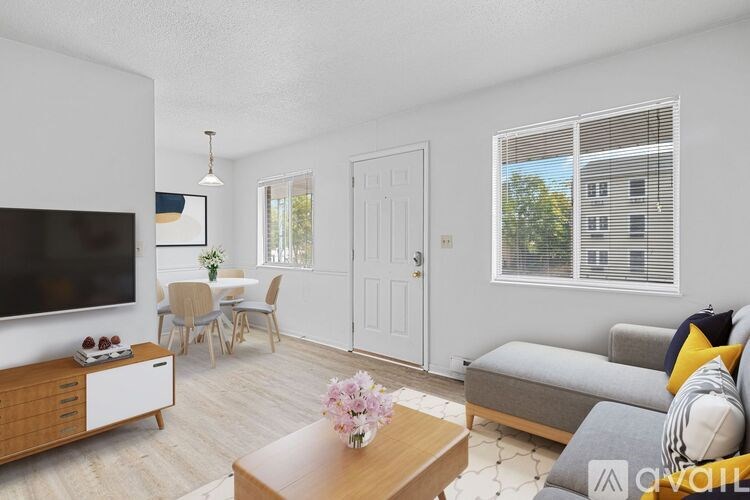 A living room with a grey couch, a wooden coffee table, a flat screen TV, and a dining table with chairs.