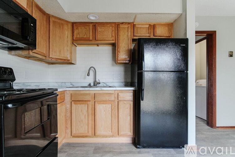 A black refrigerator is in a kitchen with wooden cabinets.