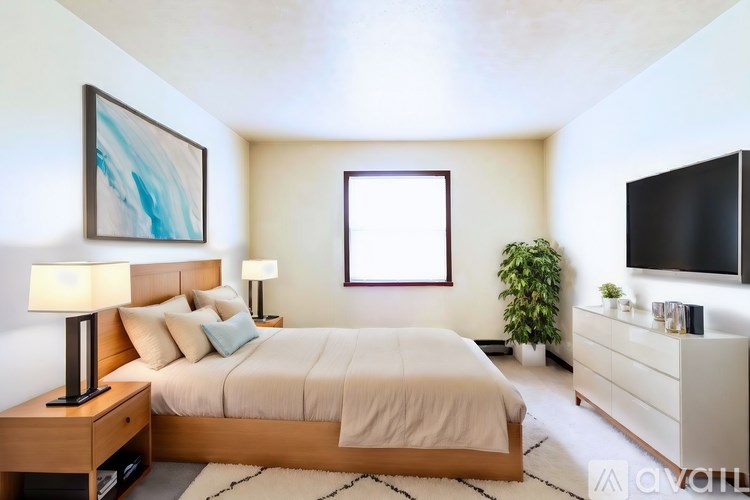 A well-lit bedroom with a large bed, a side table with a lamp, and a TV on the wall.