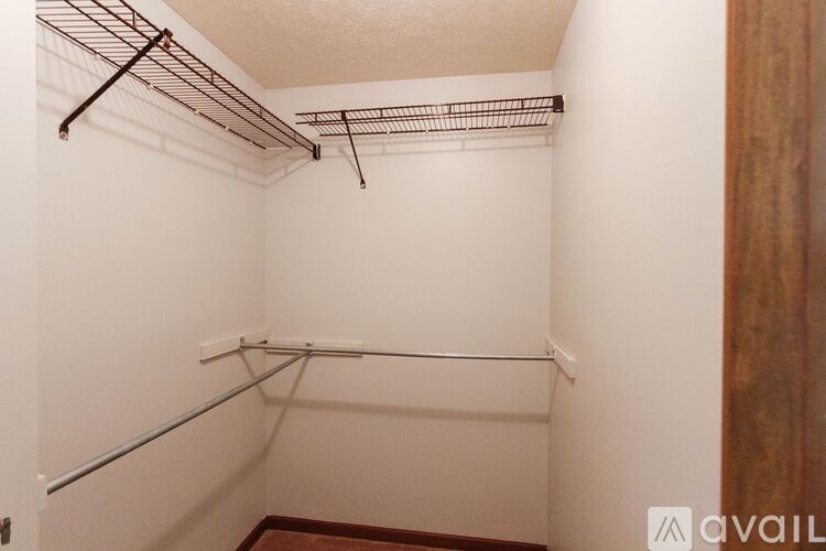 A walk-in closet with a white wall and a brown door.