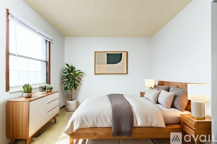 A bedroom with a bed, nightstand, and a plant.