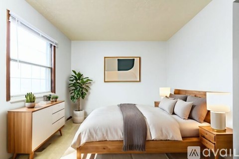 A bedroom with a bed, nightstand, and a plant.