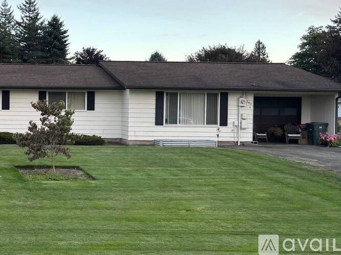 A house with a white exterior and a brown roof with a small tree in front of it.