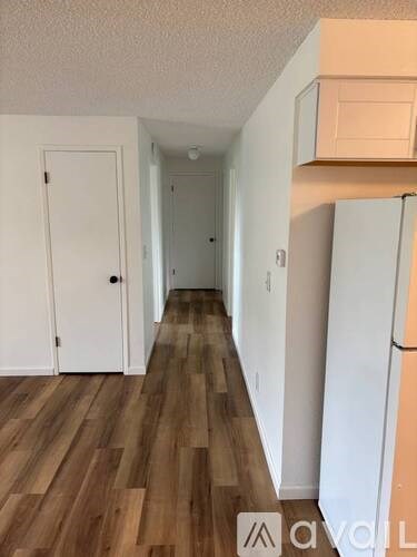 A long hallway with a white door on the left and a white refrigerator on the right.