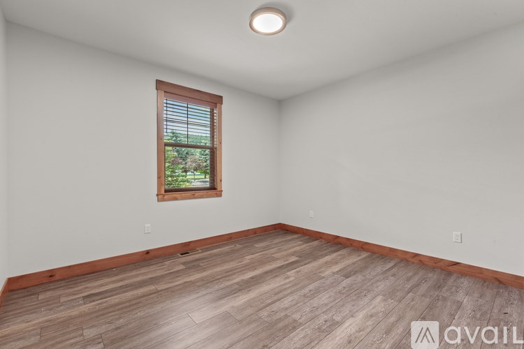 A room with wooden flooring and a window showing greenery outside.