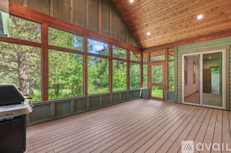 A wooden deck with a grill and a window overlooking a forest.