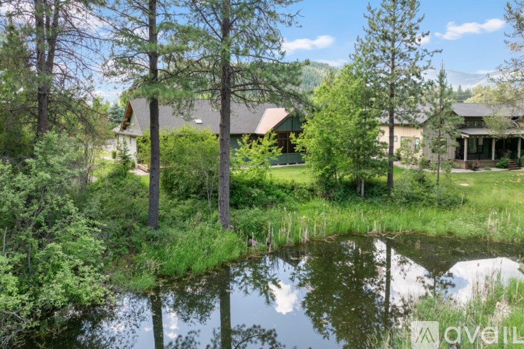 A serene landscape with a pond, trees, and houses.