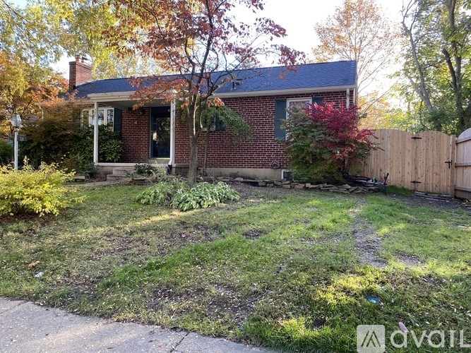 A house with a red brick exterior and a blue roof is surrounded by a wooden fence and greenery.