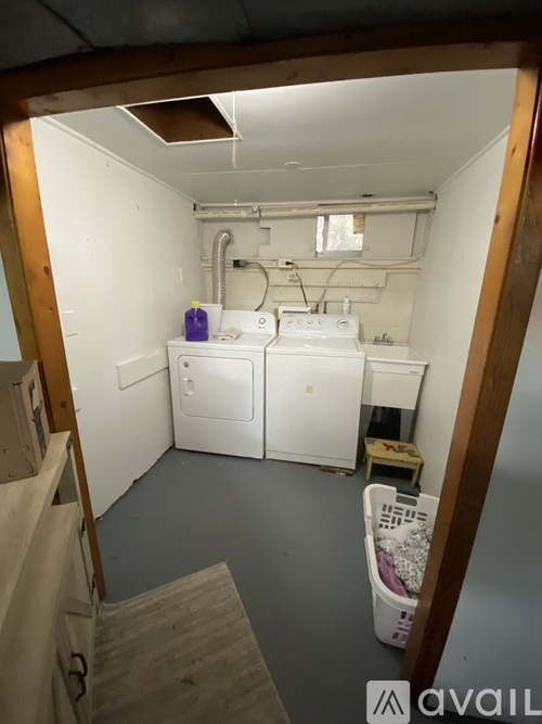 A small, white, and wooden bathroom with a toilet, sink, and a trash can.