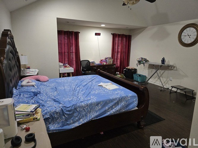 A bedroom with a bed, desk, chair, and a clock on the wall.