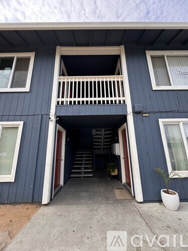 A blue house with a white balcony and a small tree in a white pot.