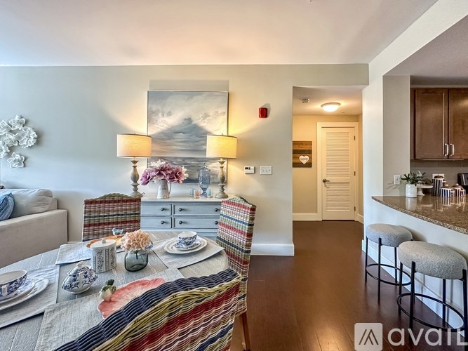 A dining room with a table set for two and a kitchen area with a bar stool.