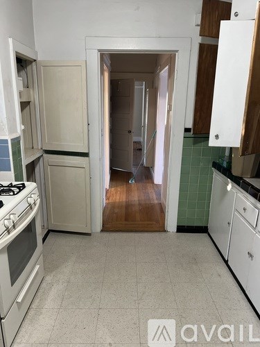 A kitchen with a white stove and cabinets with a door open to a hallway.