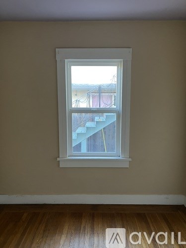A window with a white frame in a room with wooden flooring.