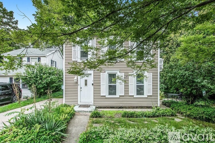 A small house with a white door and windows is surrounded by greenery.