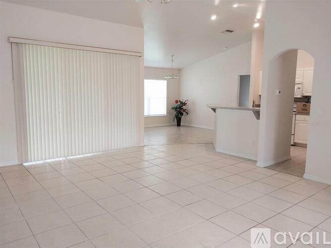 A spacious room with tiled flooring and three windows with black curtains.