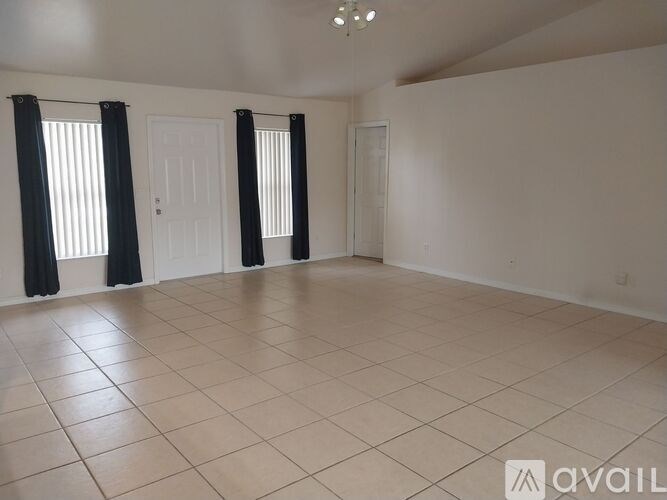 A spacious room with tiled flooring and three windows with black curtains.
