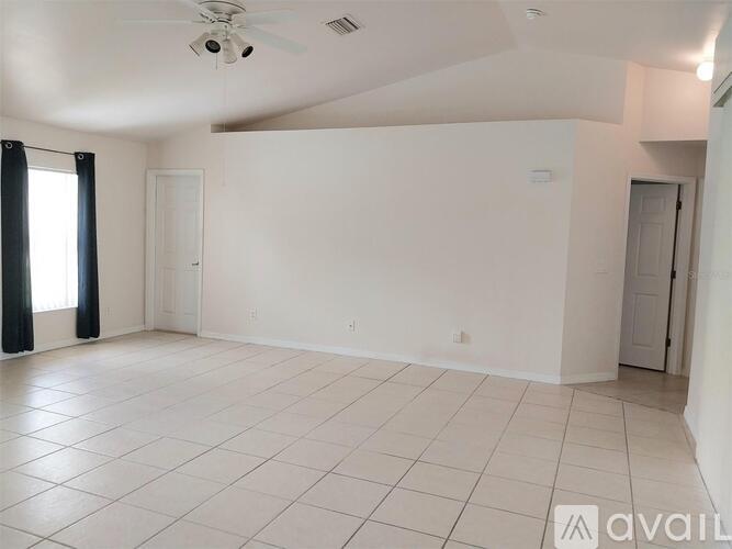 A spacious, empty room with white tiled flooring and a large window with blinds.