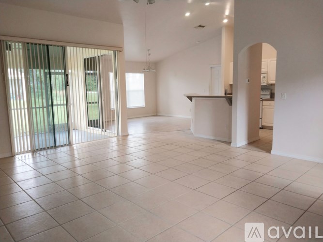 A spacious, empty room with white tiled flooring and a large window with blinds.